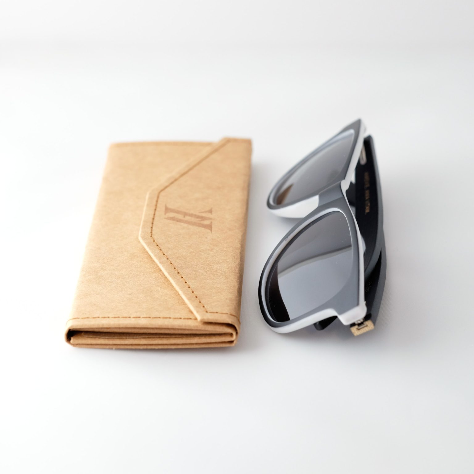 Bamboo sunglasses , folded, next to folded case . Dark grey lenses, polarized, and matte black and white frame. Designed in Canada