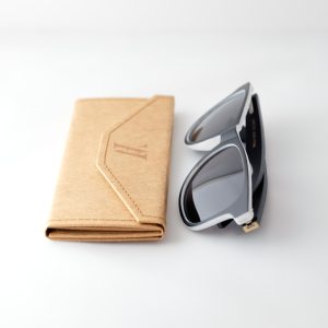 Bamboo sunglasses , folded, next to folded case . Dark grey lenses, polarized, and matte black and white frame. Designed in Canada