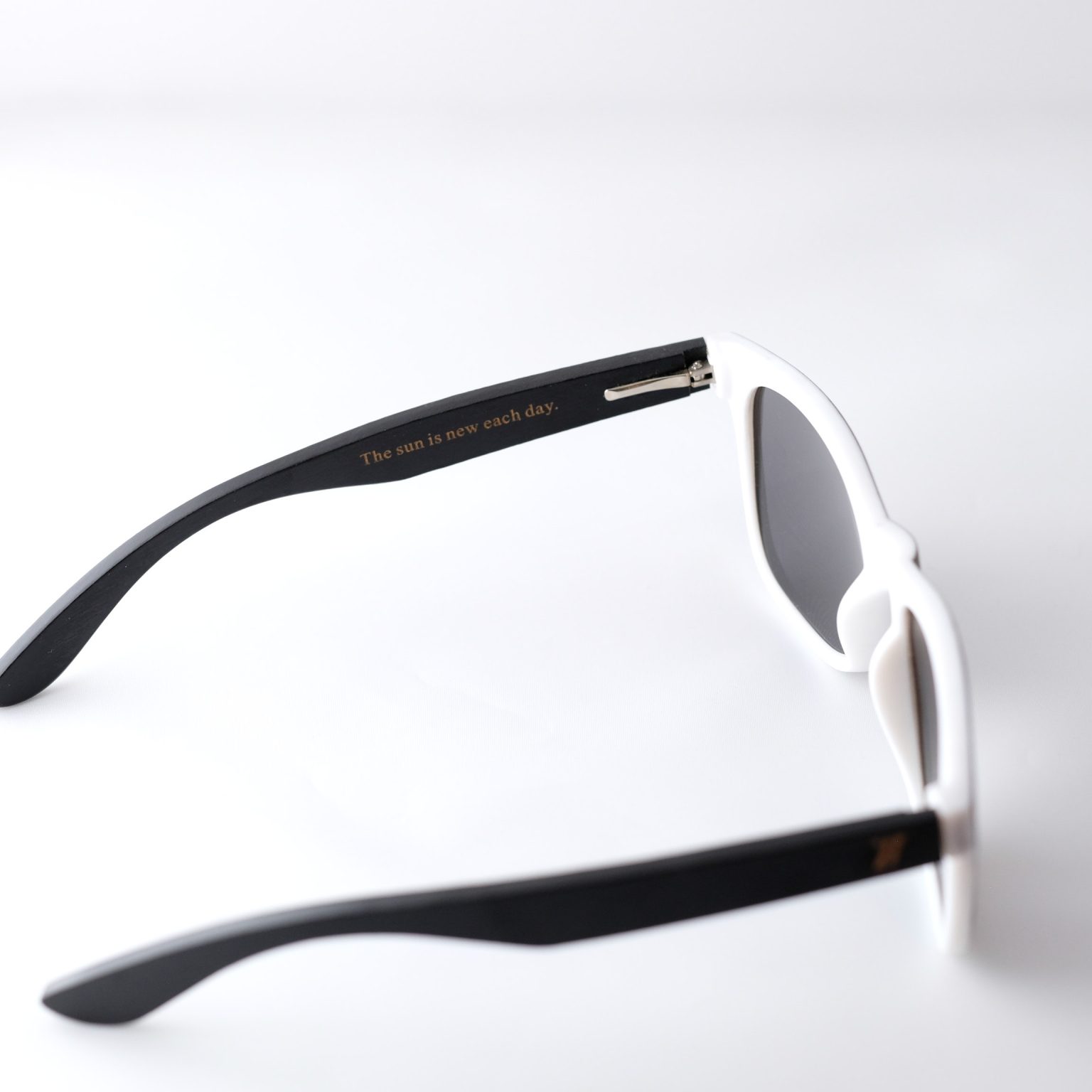 Bamboo sunglasses , folded out. The arm reads : " the sun is new each day"Dark grey lenses, polarized, and matte black and white frame. Designed in Canada
