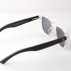 Bamboo sunglasses open on white background, white frames, grey lenses and black arms. On the inside of one arm it is engraved : 