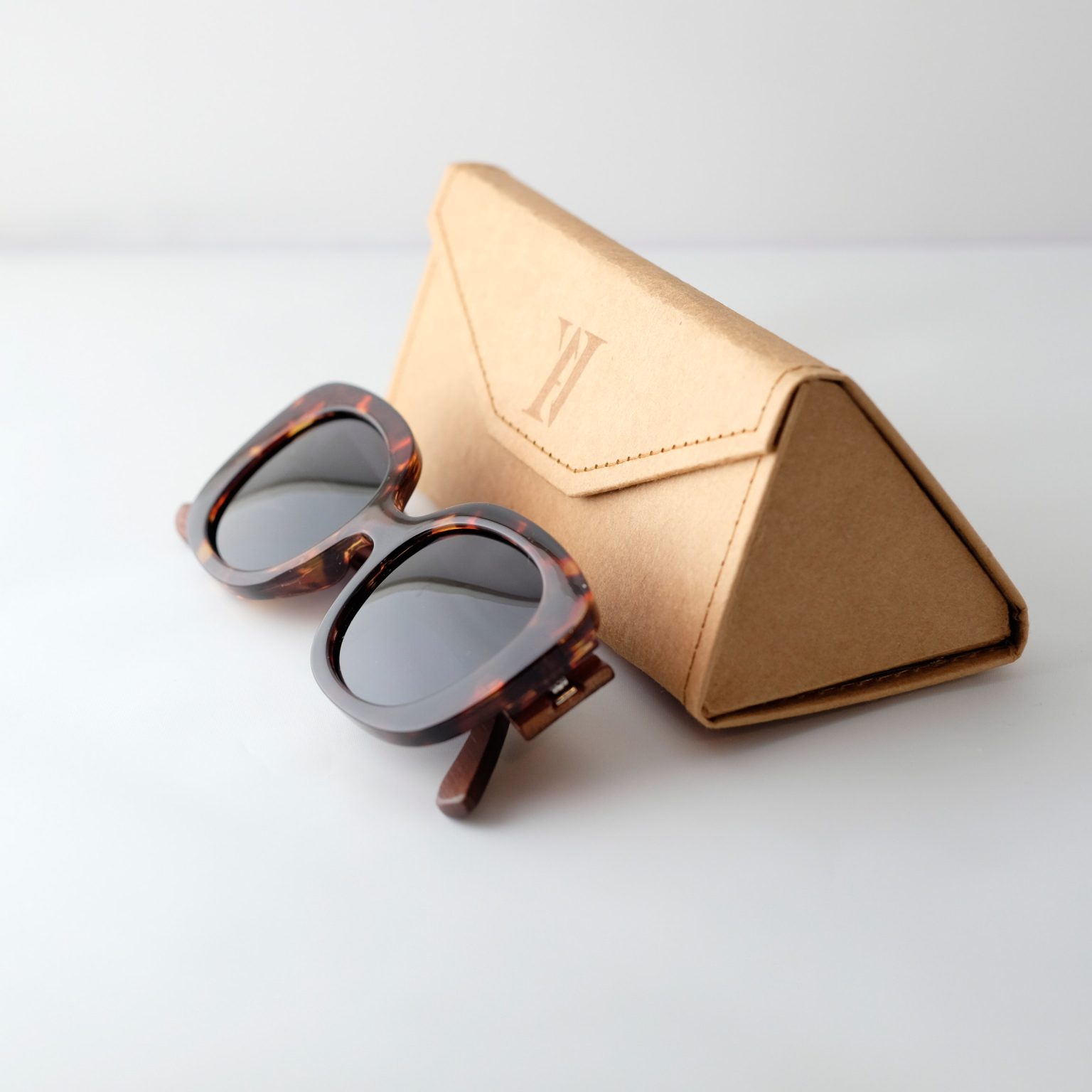 Bucharest night bamboo sunglasses folded next to an open case, on a white background. They have grey lenses, tortoise frame and brown arms