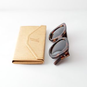 Bucharest night bamboo sunglasses folded next to a folded case, on a white background. They have grey lenses, tortoise frame and brown arms