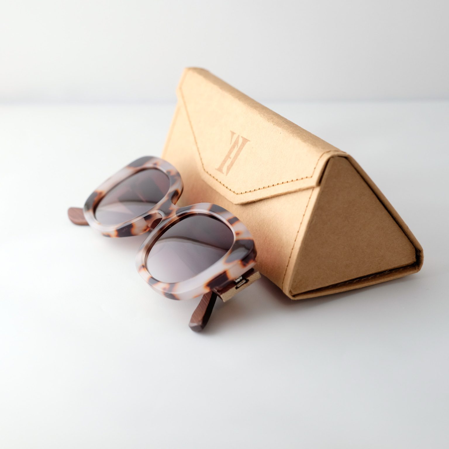 Bucharest Sunrise bamboo sunglasses folded next to case on a white background. They have brown lenses, tortoise frame and brown arms