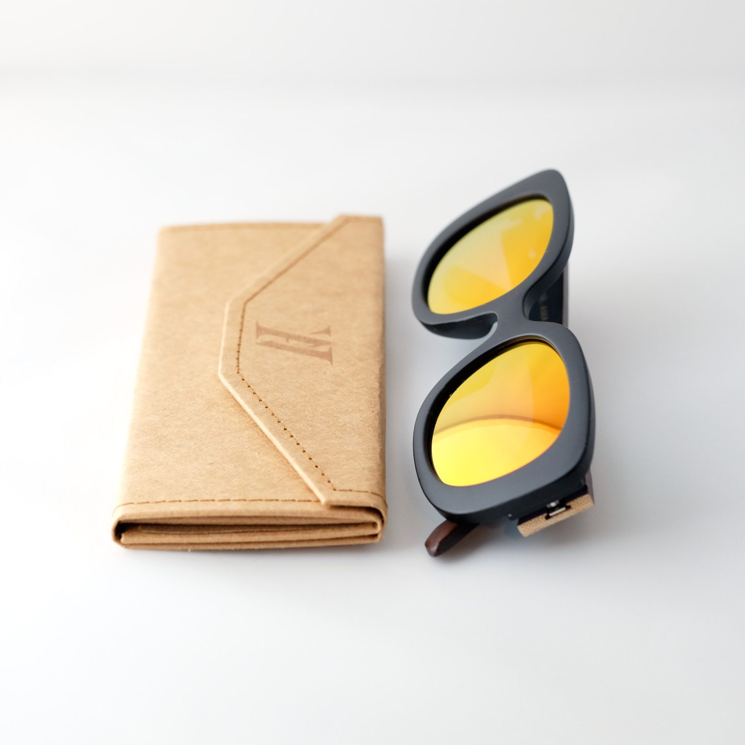 Bucharest Sunset bamboo sunglasses folded next to folded case, on a white background. They have orange reflective lenses, black frame and brown arms