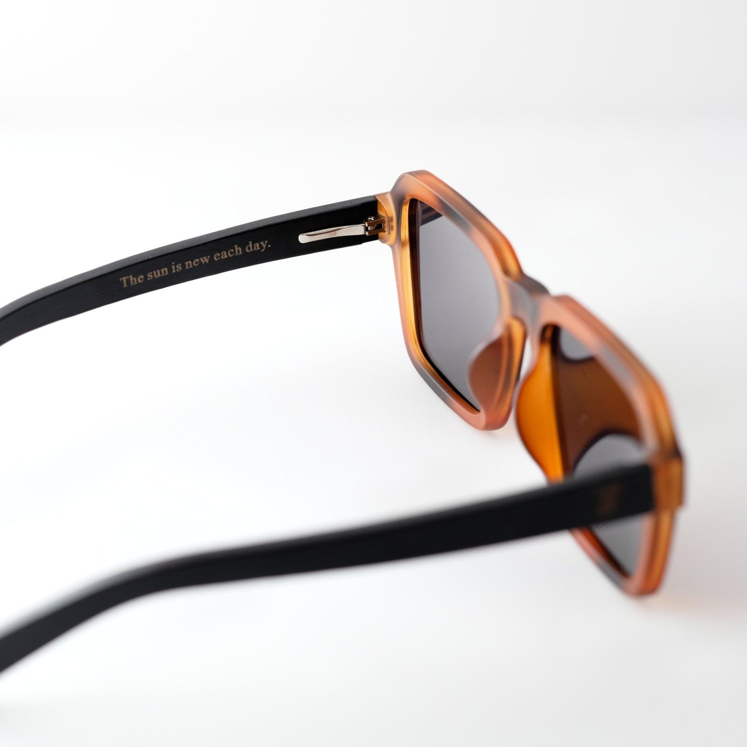 Carpathia bamboo sunglasses opened on a white background, with tortie frame, brown lenses and black brown natural bamboo arms. the inside arm reads "the sun is new each day"
