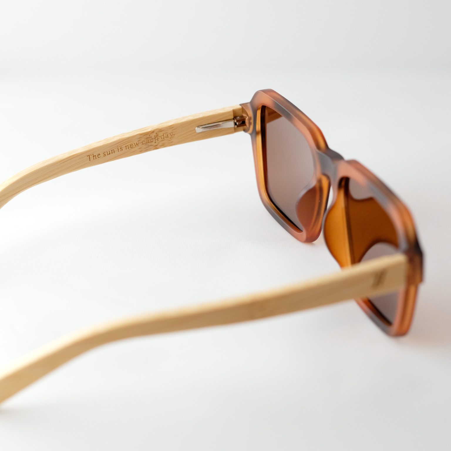 Carpathia bamboo sunglasses opened on a white background, with tortie frame, brown lenses and light brown natural bamboo arms. The inside of the arm reads "the sun is new each day"