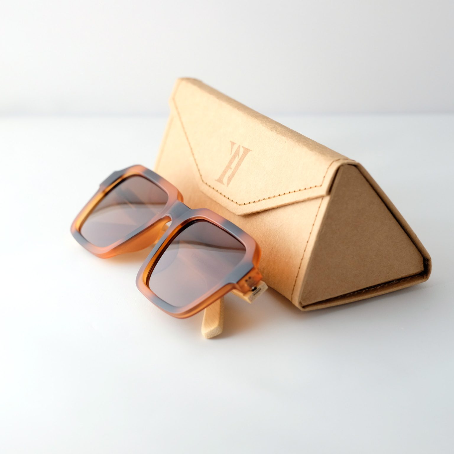 Carpathia bamboo sunglasses folded next to their case on a white background, with tortie frame, brown lenses and light brown natural bamboo arms.