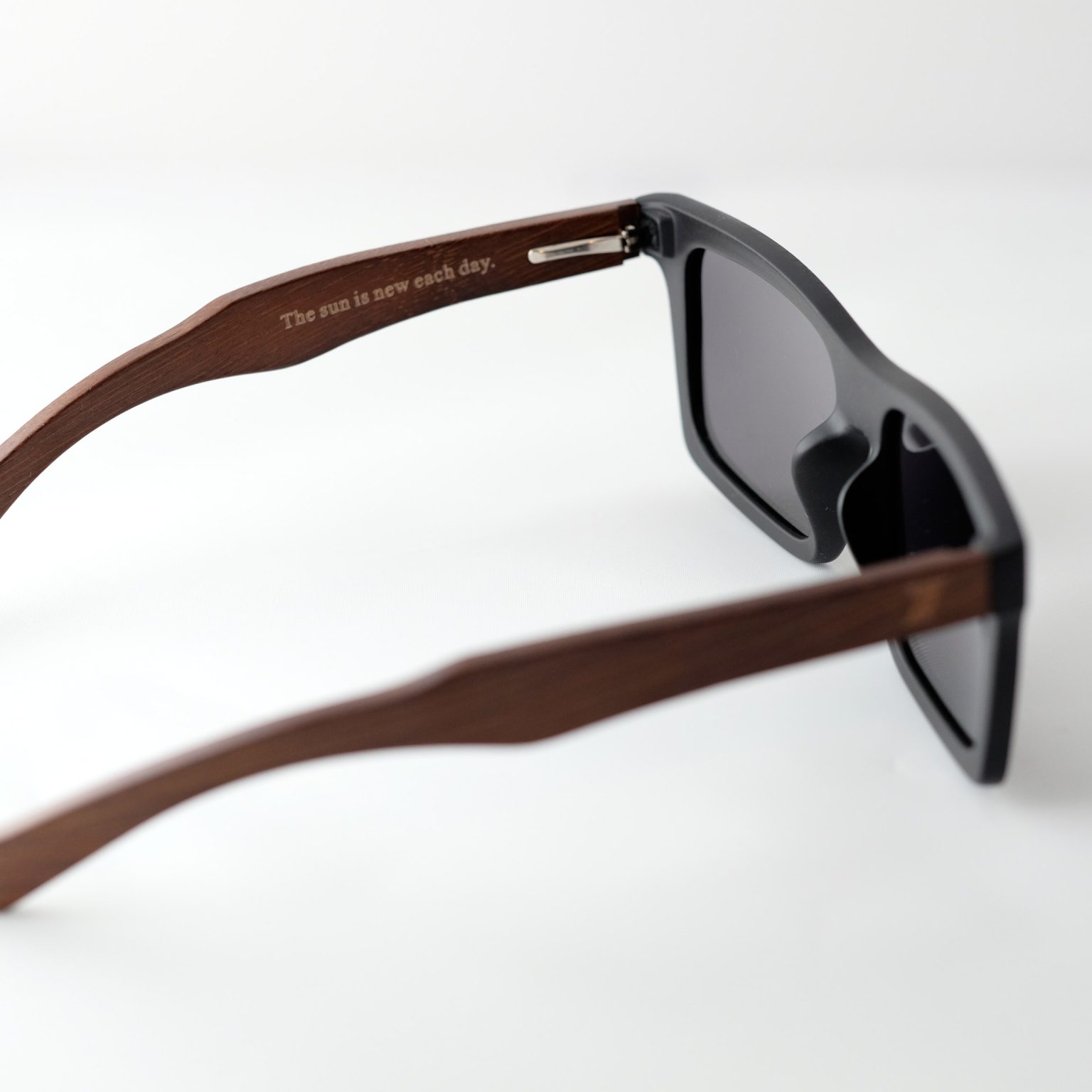 bamboo sunglasses on white background, with brown arms and matte black frames. Smokey dark grey lenses. Inside arm reads " The sun is new each day" Designed in Canada