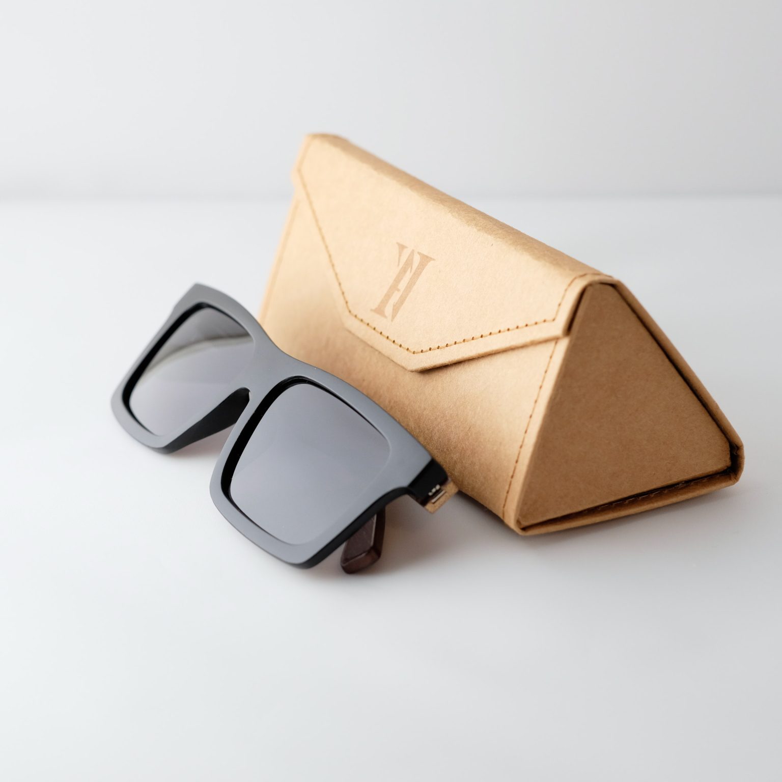 bamboo sunglasses on white background, next to case; with brown arms and matte black frames. Smokey dark grey lenses. Designed in Canada