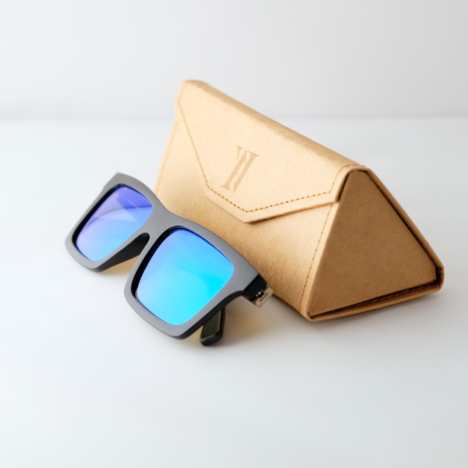 bamboo sunglasses on white background, set next to a case; with black arms and matte black frames. blue reflective lenses. Designed in Canada