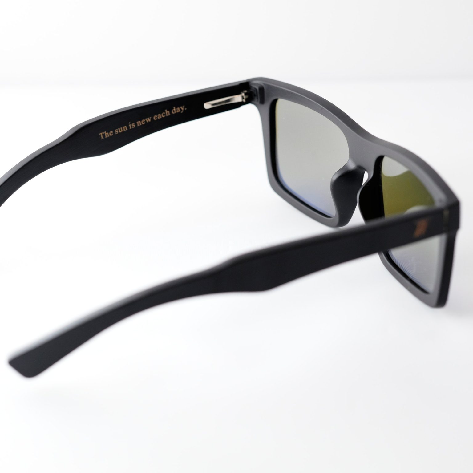 bamboo sunglasses on white background, with black arms and matte black frames. Arms read " the sun is new each day" engraved; blue reflective lenses. Designed in Canada